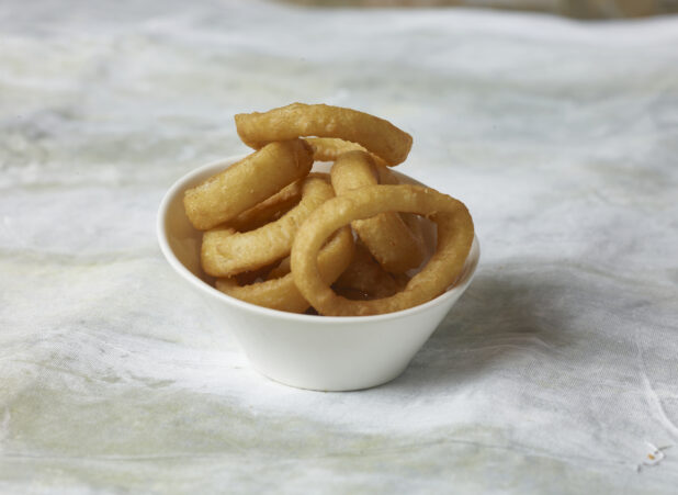 Onion rings in a small round white bowl on a canvas background