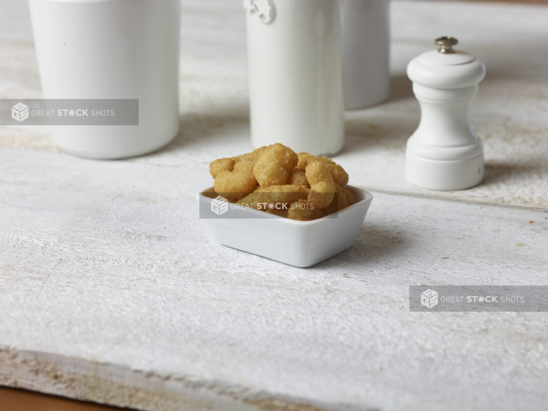 Popcorn shrimp in a small square white bowl on a white wooden table with white accessories in the background