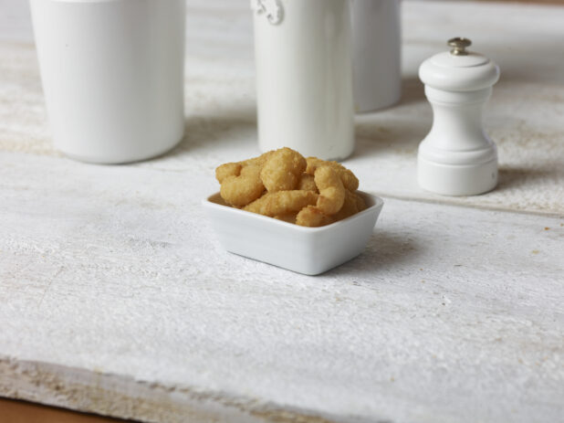Popcorn shrimp in a small square white bowl on a white wooden table with white accessories in the background