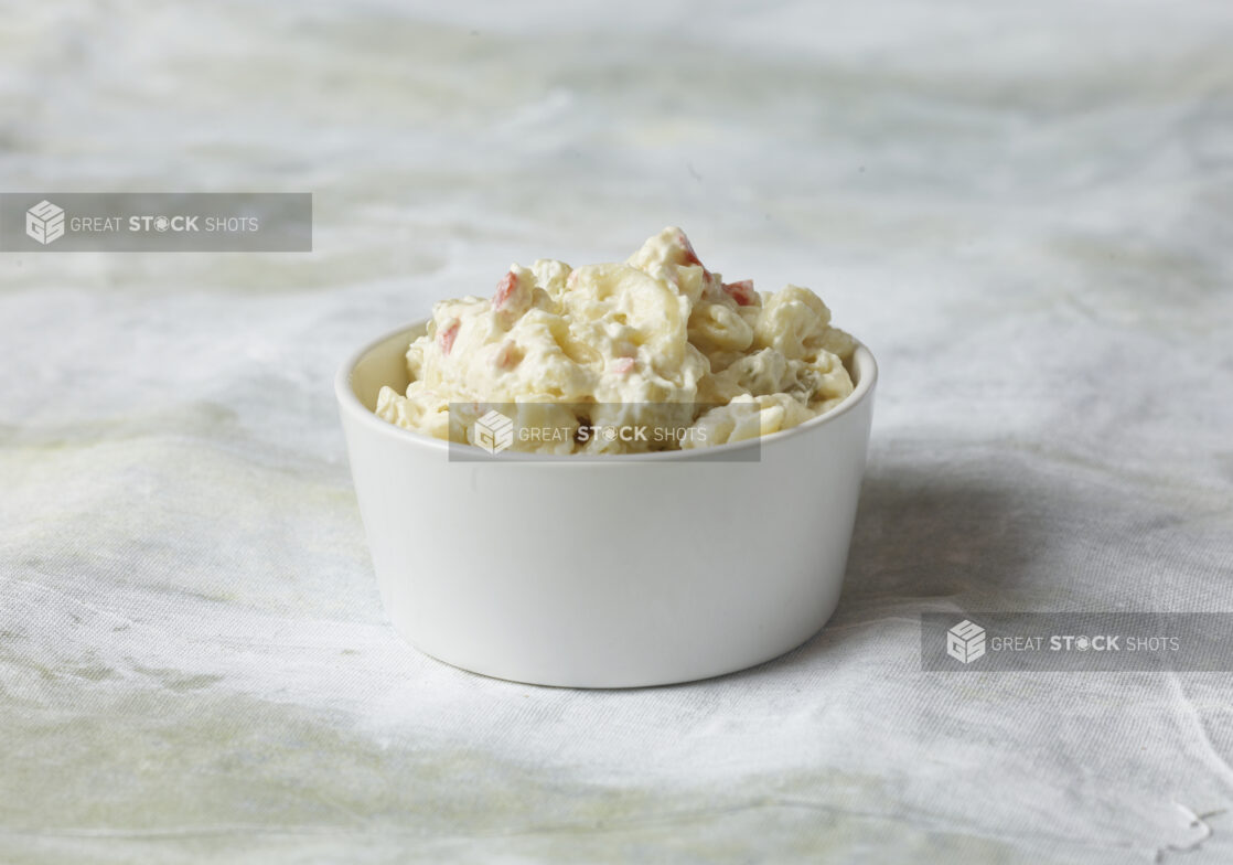 Side potato salad in a small white bowl, close up view on a white canvas background