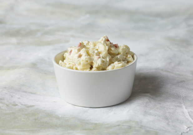 Side potato salad in a small white bowl, close up view on a white canvas background