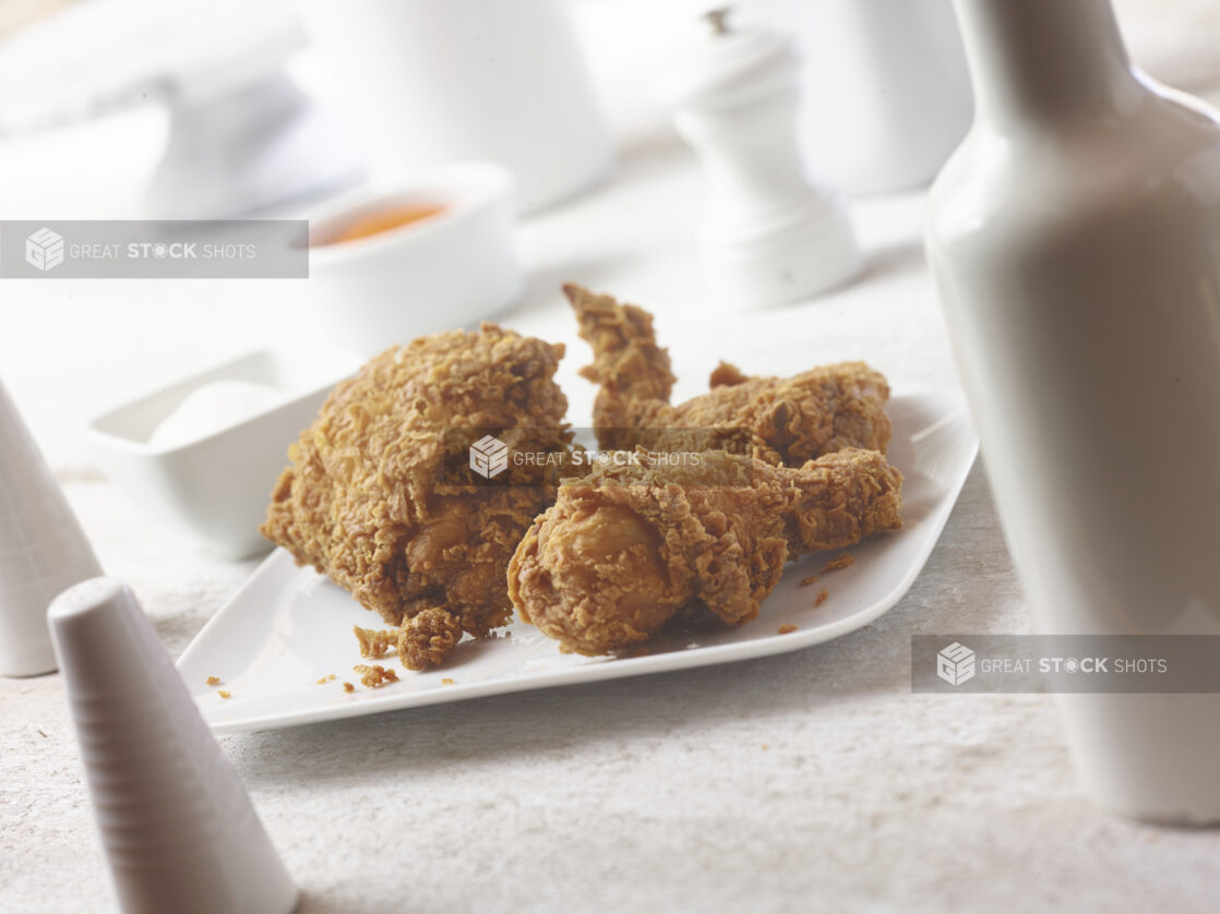 45 degree angle of fried chicken on a square white plate with white accessories in the background