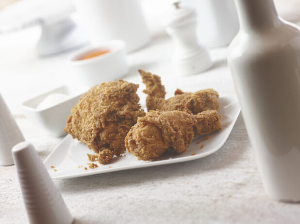 45 degree angle of fried chicken on a square white plate with white accessories in the background