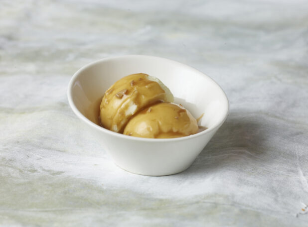 Close up view of mashed potato side dish with gravy in a small white bowl on a canvas background