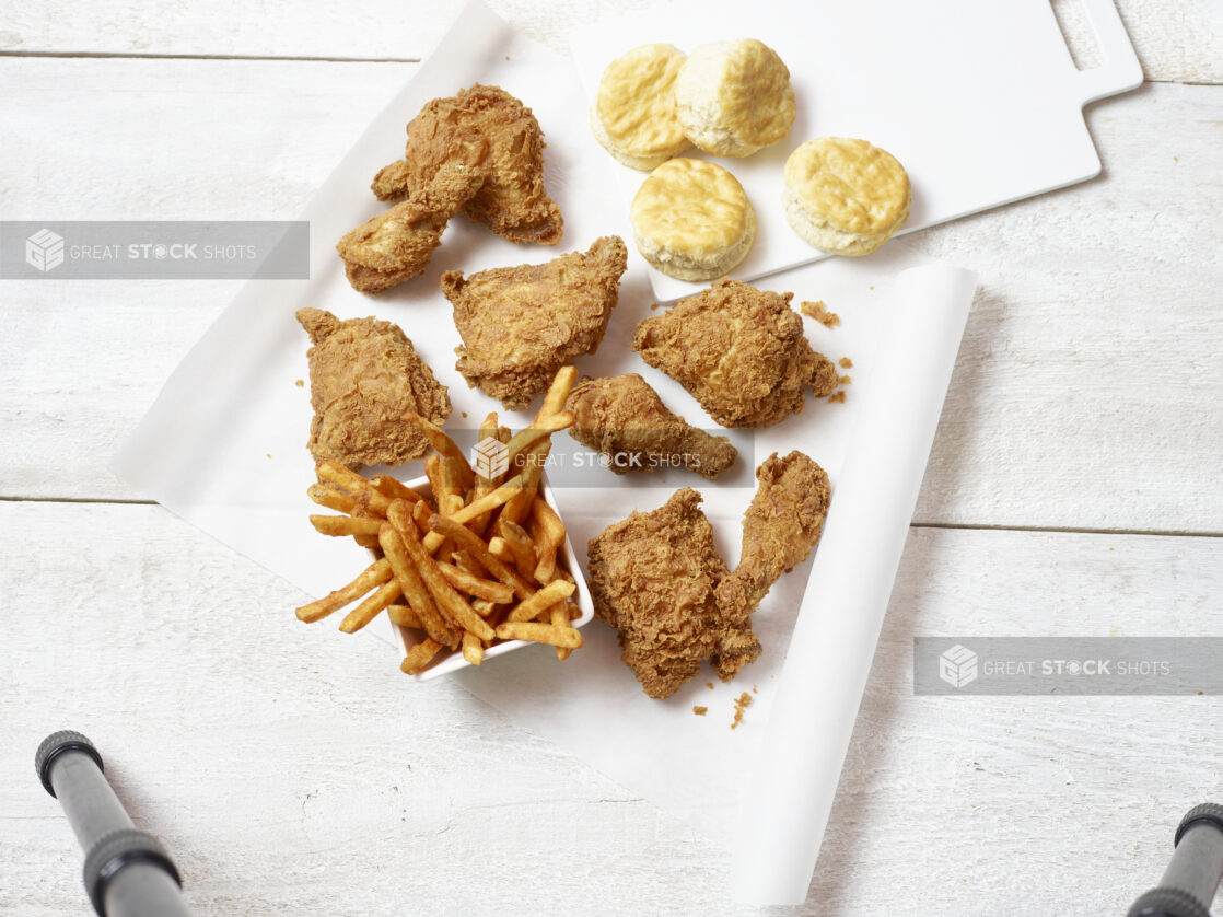 Overhead view of fried chicken, side bowl of french fries and biscuits on a white background