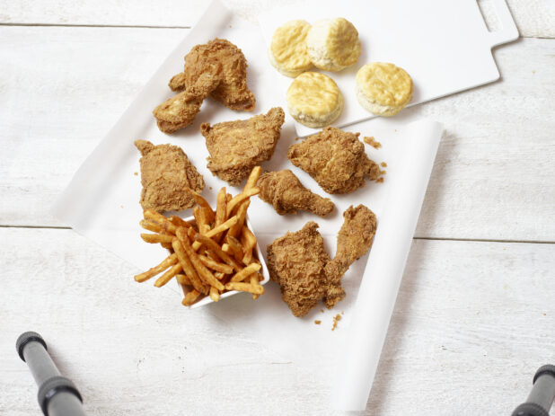 Overhead view of fried chicken, side bowl of french fries and biscuits on a white background