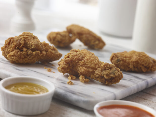 4 breaded  chicken wings displayed on a marble board with 2 dipping sauces in white ramekins, close up view