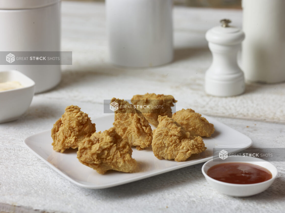 Fried chicken on a rectangular white platter with a ramekin of ketchup in the forefront with white accessories in the background