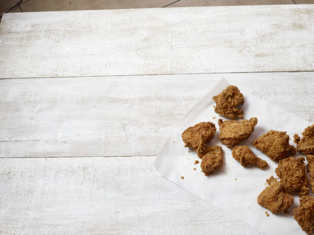 Overhead, off center view of fried chicken on parchment paper on a white wooden table