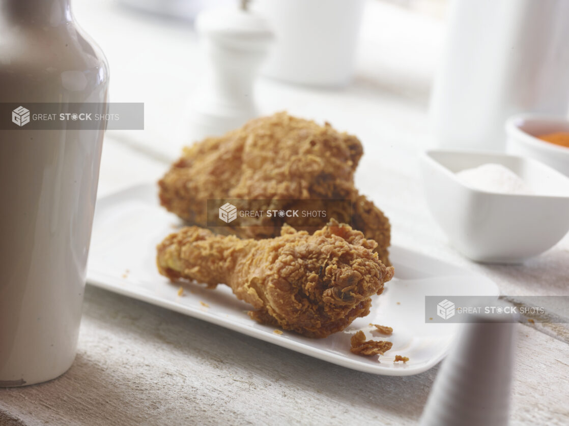 Close up view fried chicken on a white side plate with white accessories surrounding