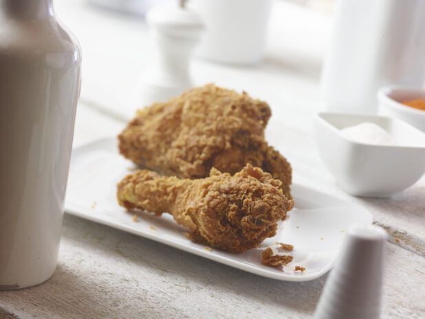 Close up view fried chicken on a white side plate with white accessories surrounding