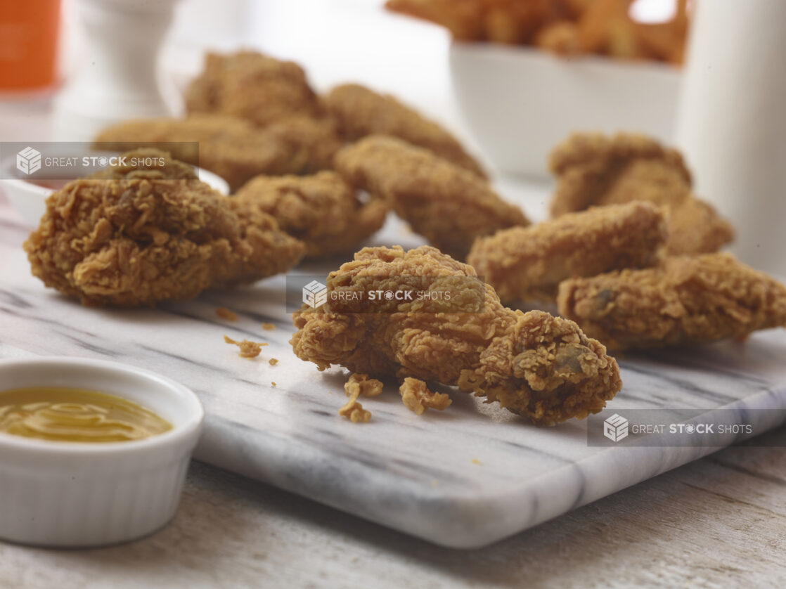 Fried chicken wings on a marble board, with dip in a ramekin in the foreground with side of sweet potato fries in the background