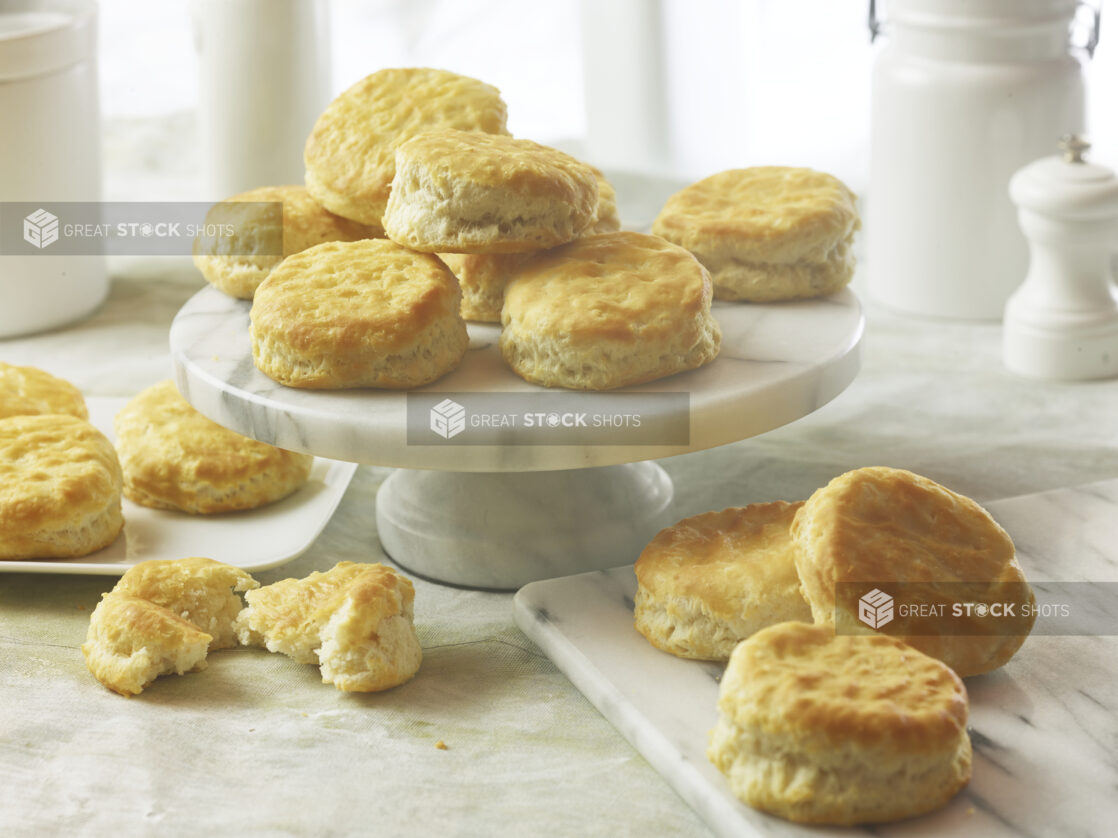 Baked biscuits/scones on a marble cake stand and on a marble cutting board and a white side plate with white accessories in the background