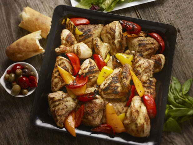 Overhead view of a square black platter of grilled chicken and bell peppers
