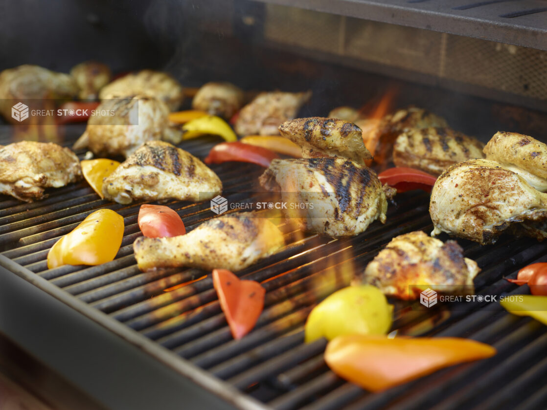 Grilled pieces of chicken and bell peppers on a BBQ with flames