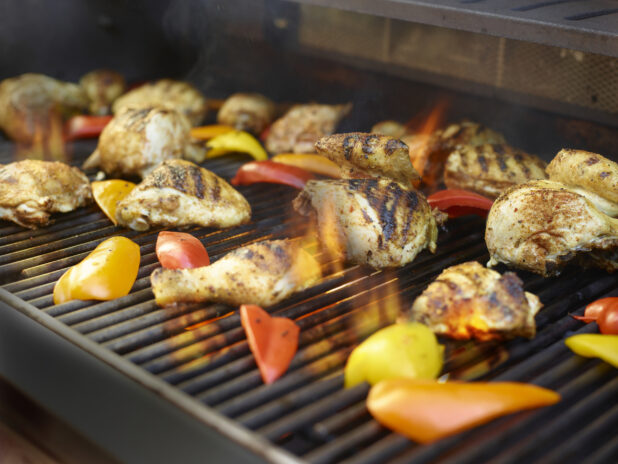 Grilled pieces of chicken and bell peppers on a BBQ with flames