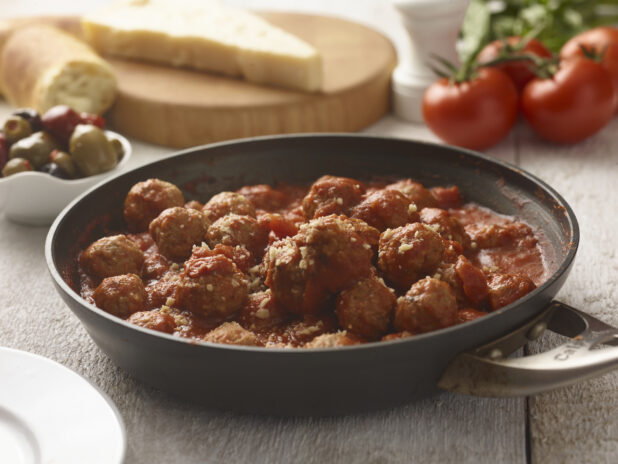 Saucepan of meatballs in tomato sauce on a whitewashed wood tabletop, fresh Italian ingredients surrounding, close-up