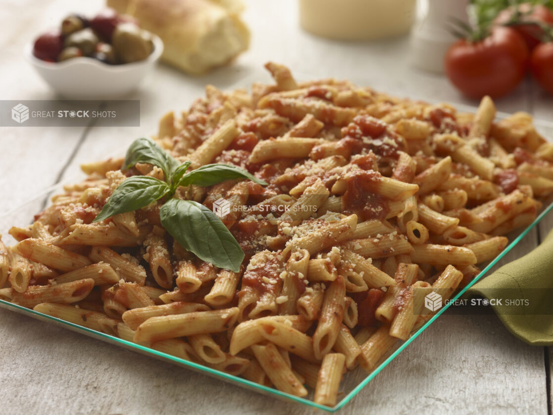 Large glass platter of penne pasta in a tomato sauce with basil garnish