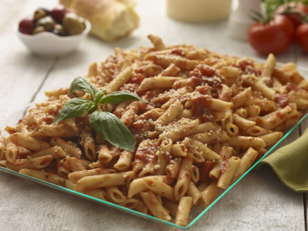 Large glass platter of penne pasta in a tomato sauce with basil garnish