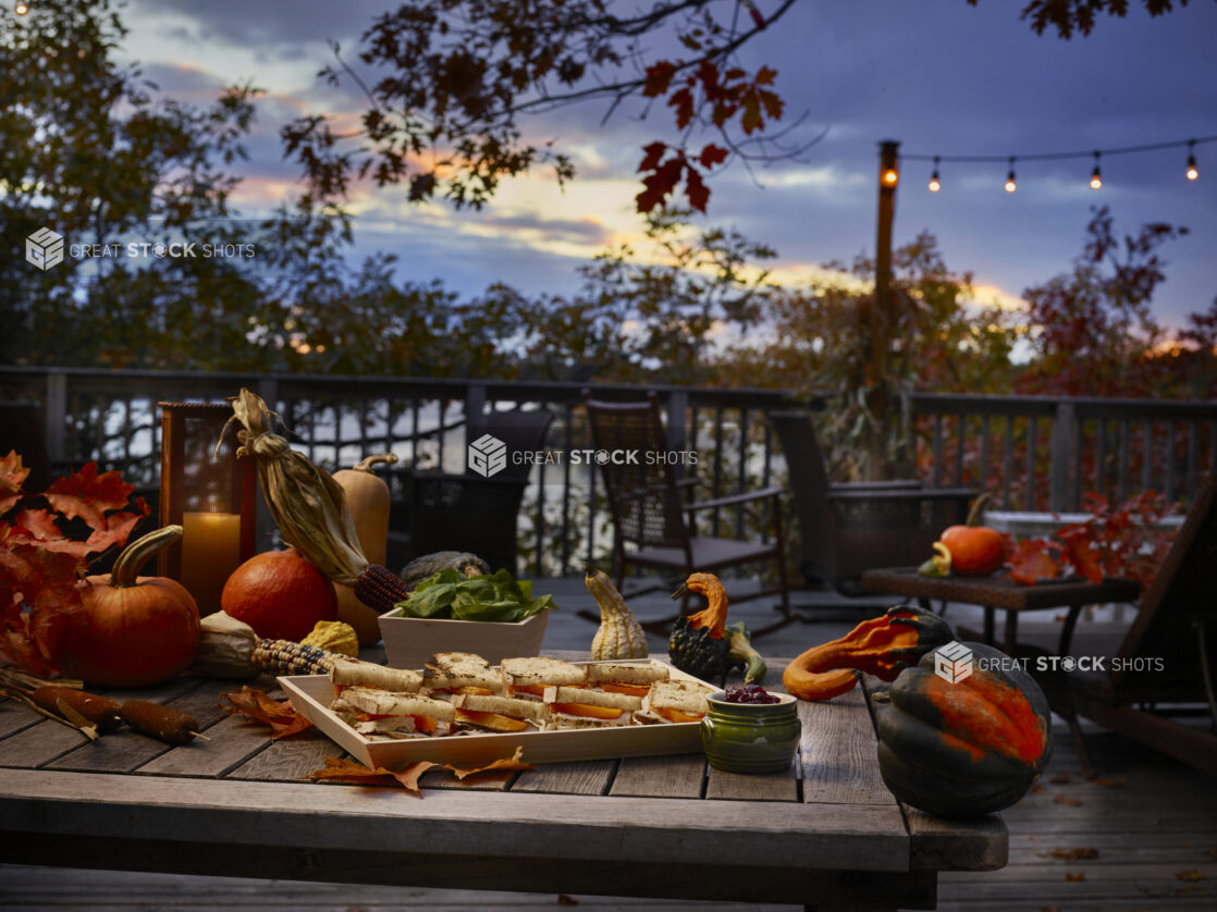 Platter of sandwiches on a wood tray in a fall-themed background with pumpkins, gourds and festive corn