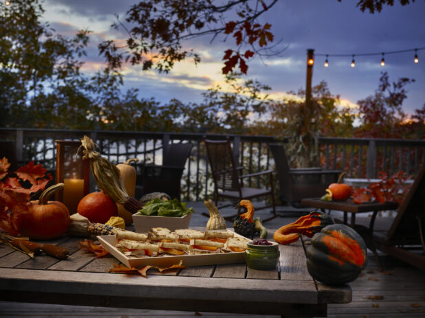 Platter of sandwiches on a wood tray in a fall-themed background with pumpkins, gourds and festive corn