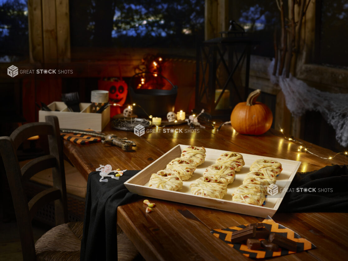 Hallowe'en Mummy mini pizzas on a wood tray on a wooden table with Hallowe'en decorations in the background and foreground