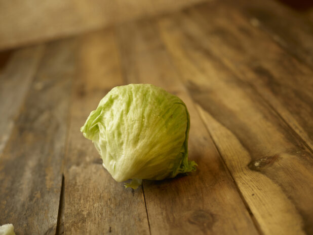 whole head of iceberg lettuce centered on an aged wooden table,