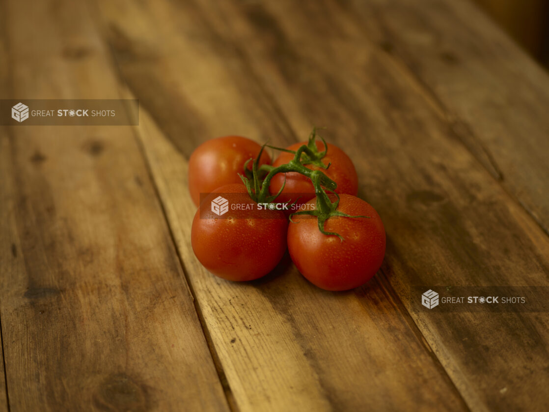 Whole ripe tomatoes on the vine on a rustic wooden table