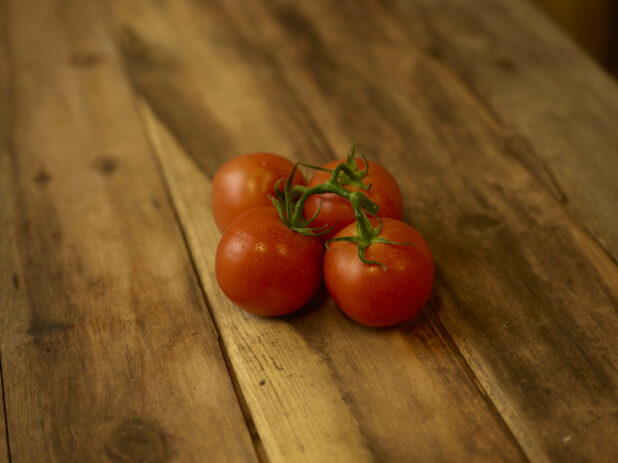 Whole ripe tomatoes on the vine on a rustic wooden table