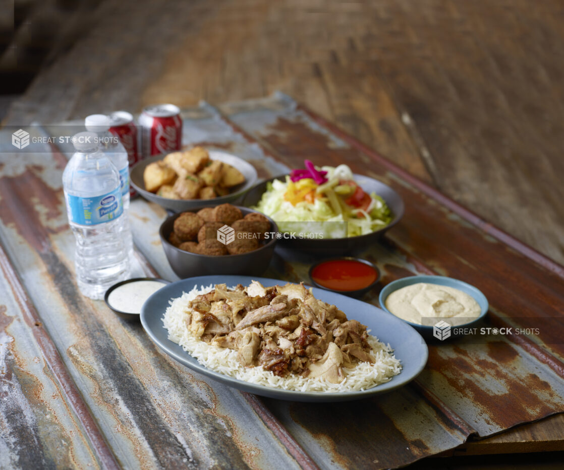 Chicken shawarma on rice with sides of salad, falafel, potatoes, hummus, water and Coke cans