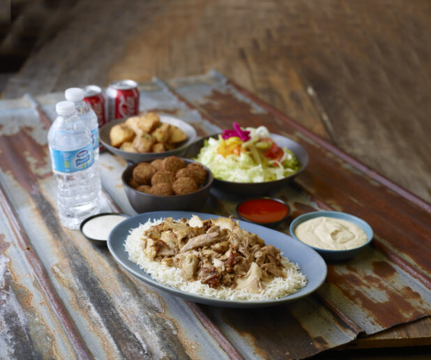 Chicken shawarma on rice with sides of salad, falafel, potatoes, hummus, water and Coke cans