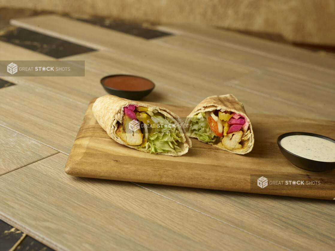 Chicken kabob wrap on a wooden cutting board with dipping sauces