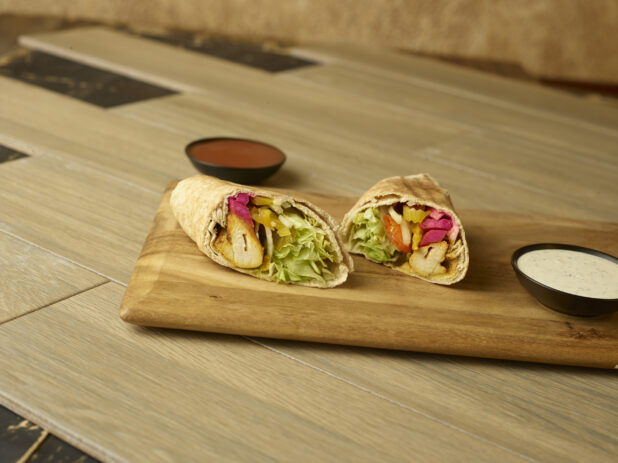 Chicken kabob wrap on a wooden cutting board with dipping sauces