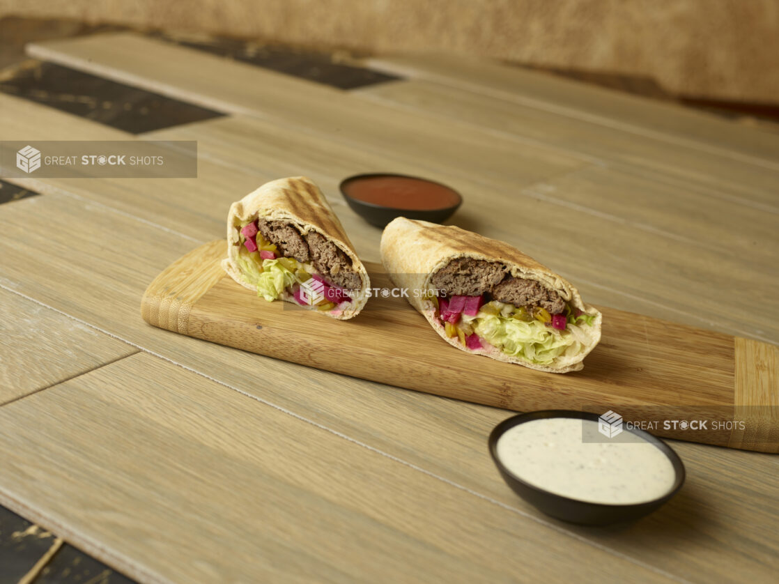 Kafta wrap on a wooden cutting board with dipping sauces