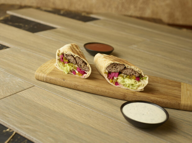 Kafta wrap on a wooden cutting board with dipping sauces