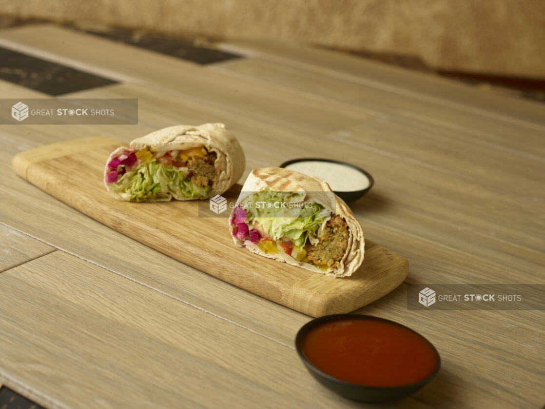 Falafel wrap on a wooden cutting board with dipping sauces