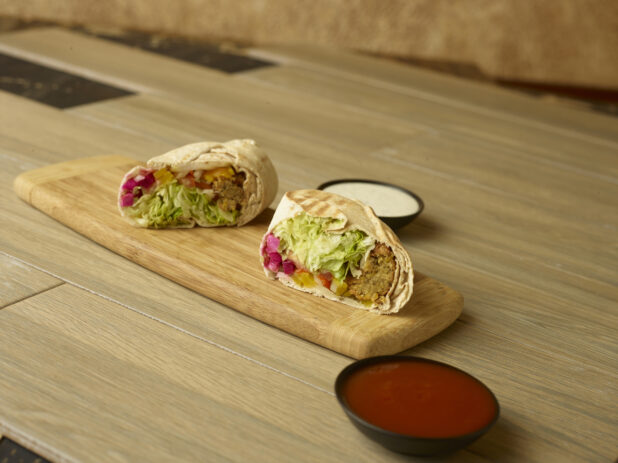 Falafel wrap on a wooden cutting board with dipping sauces