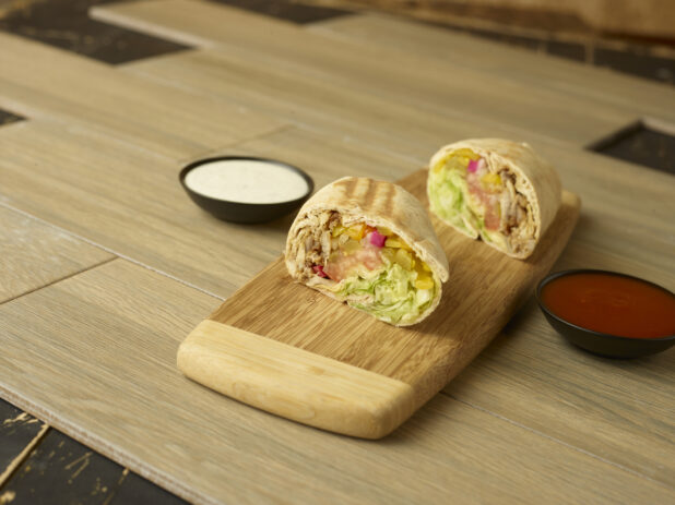 Chicken shawarma wrap on a wooden cutting board with dipping sauces