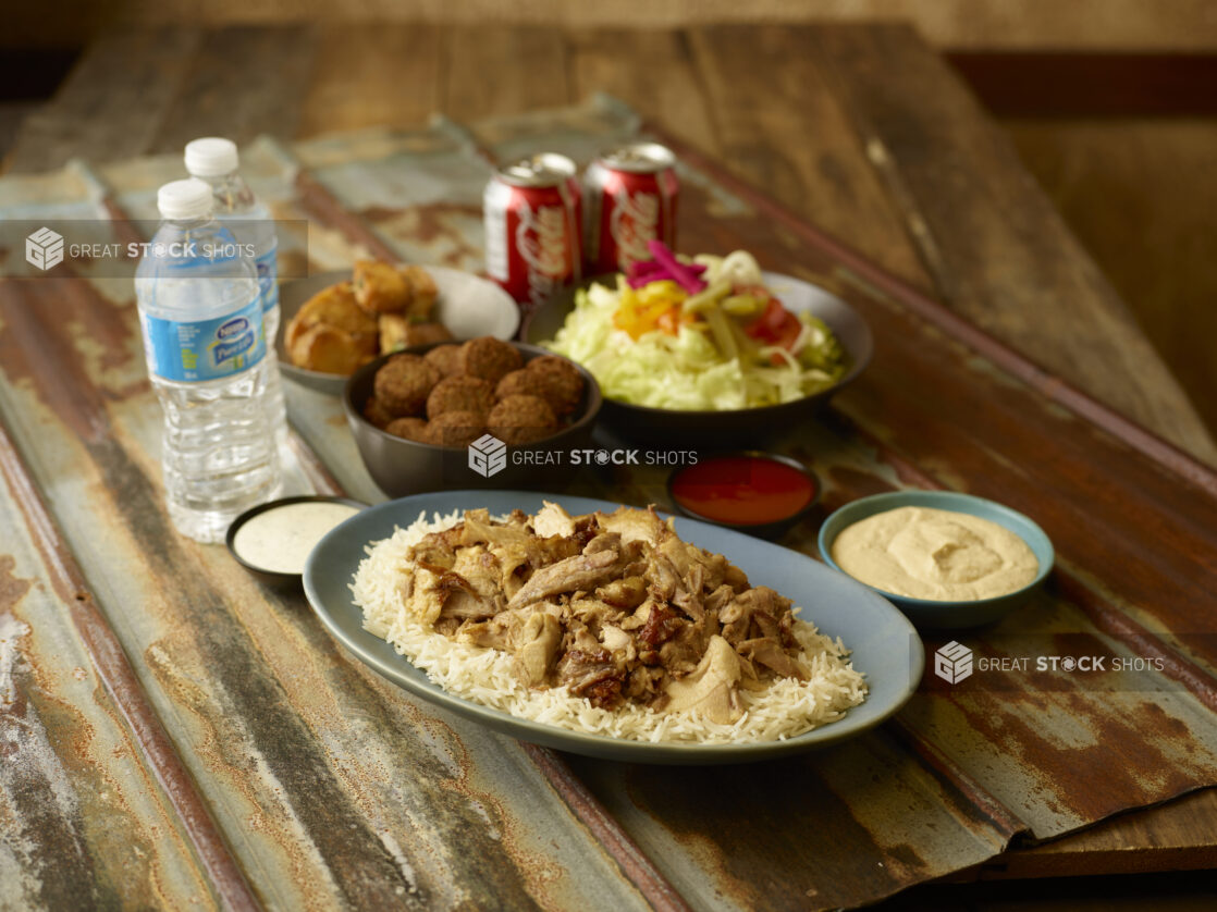 Chicken shawarma on rice with sides of salad, falafel, potatoes, hummus, water and Coke cans