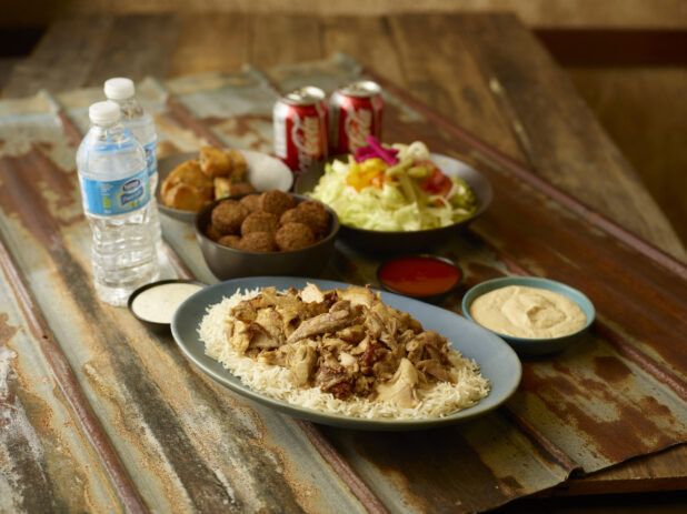 Chicken shawarma on rice with sides of salad, falafel, potatoes, hummus, water and Coke cans