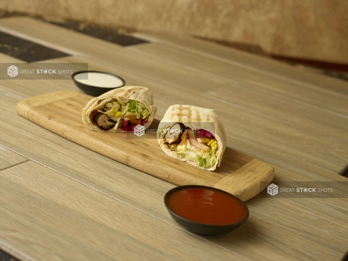 Beef and Chicken shawarma wrap, cut and displayed on a wooden cutting board on a wooden background with dips