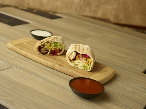 Beef and Chicken shawarma wrap, cut and displayed on a wooden cutting board on a wooden background with dips