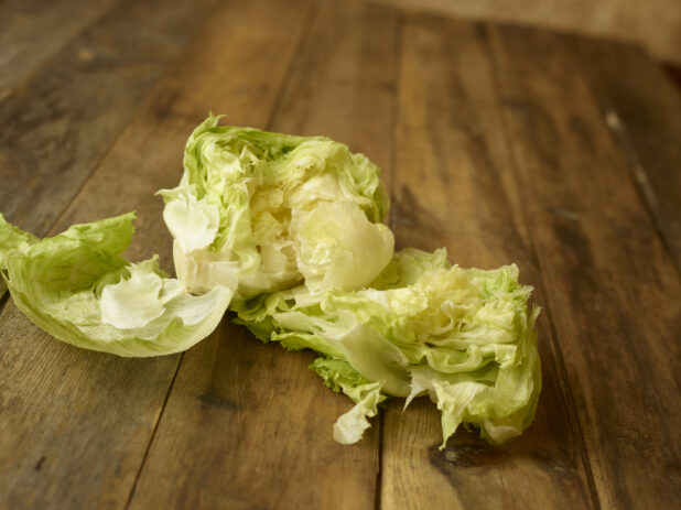 Fresh iceberg lettuce torn open on a rustic wooden table, straight on view