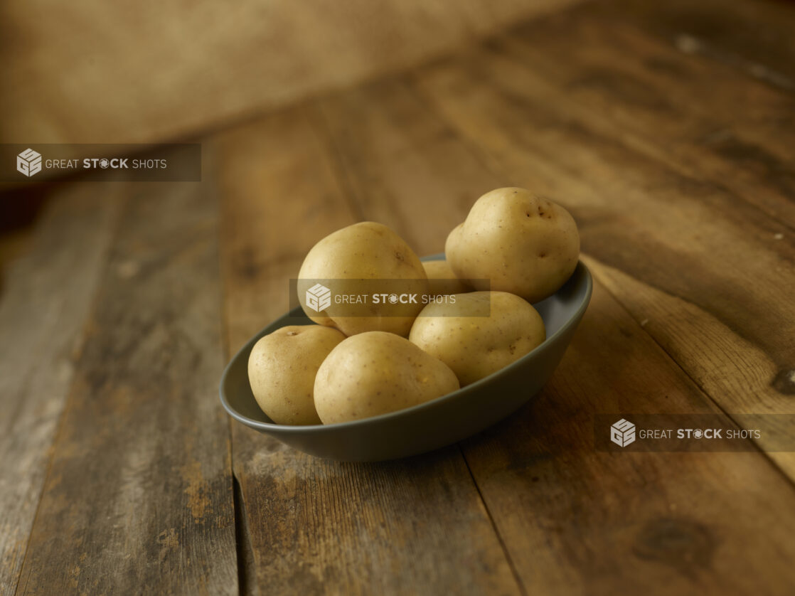 A bowl of whole/uncooked potatoes on a rustic wooden table on a 45 degree angle