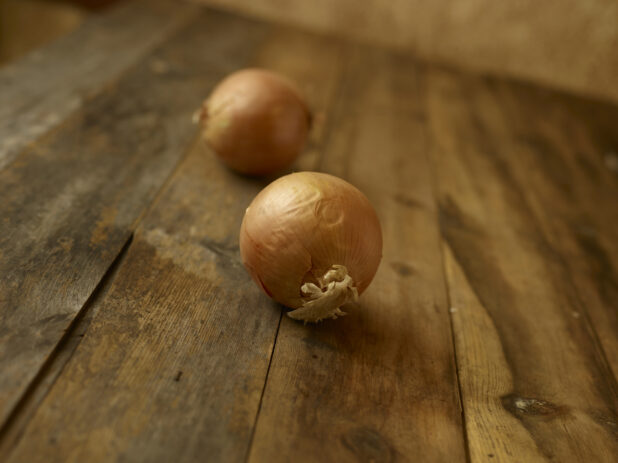 Whole uncooked onions on a rustic wooden table on a 45 degree angle