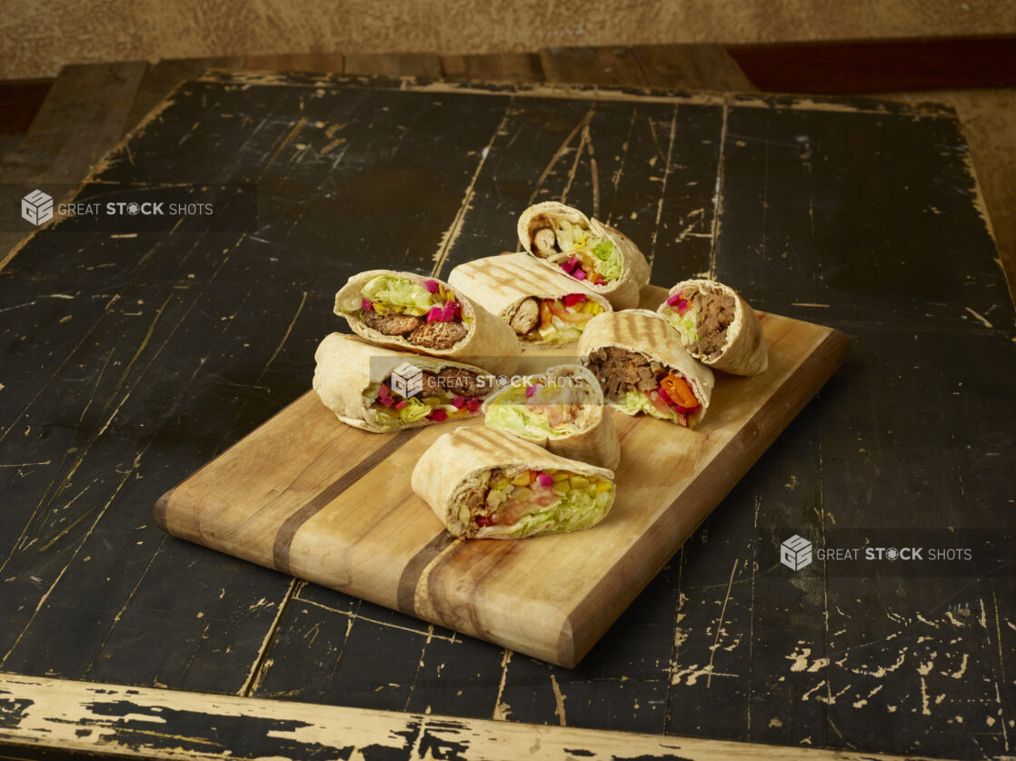 Beef and Chicken shawarma wraps, cut and displayed on a wooden cutting board on a weathered wooden background