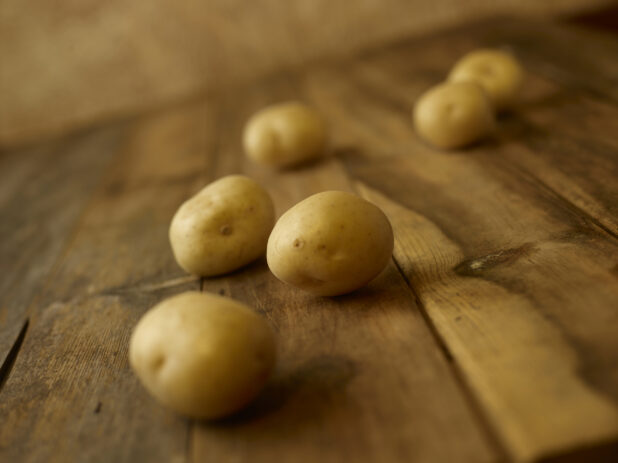 Whole uncooked potatoes on a rustic wooden table shot on a 45 degree angle