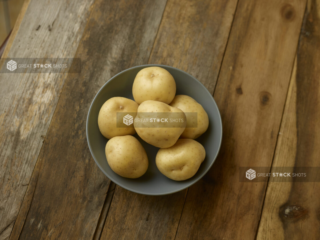 A bowl of whole/uncooked potatoes on a rustic wooden table