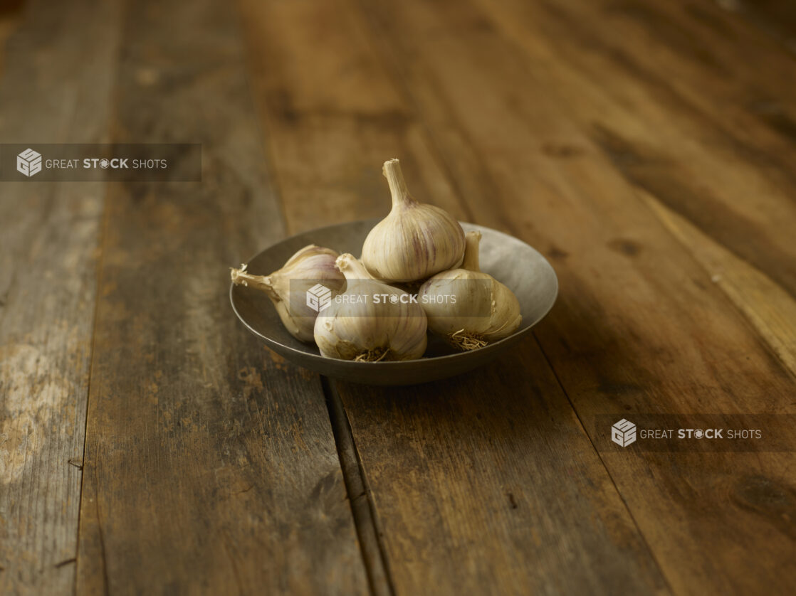 4 garlic heads in a bowl on a aged wooden table center/close up view