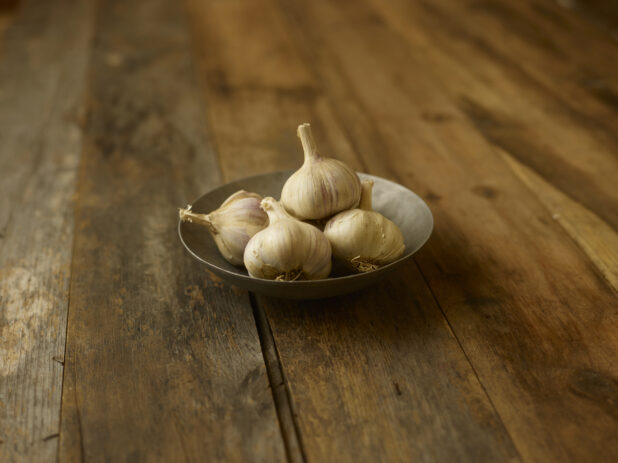 4 garlic heads in a bowl on a aged wooden table center/close up view